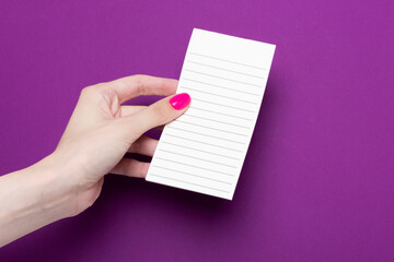 Obraz premium Female hand holds a leaf on a purple background. Hands with pink manicure. Flat lay style