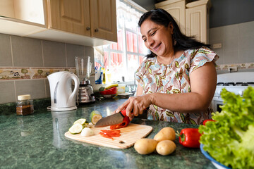 Happy Hispanic Mom Cooking Healthy Food - Mature Woman Cutting Fresh Vegetables In Her Kitchen -...
