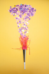 Heap of purple confetti and party horn arranged on yellow background