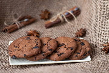 Chocolate cookies lie on a white saucer against a background of sackcloth,