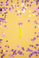 Party horn and scattered shiny confetti on orange background