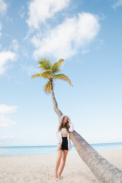 Beautiful blonde woman on the lonely tropical beach with turquoise water and white sand in the shadow of the palm tree leaf. Saona, Dominican Republic.