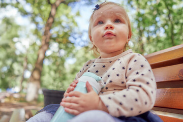 close-up portrait of an infant girl on a park bench with a thermos