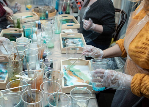 01.18.2021, Russia, St. Petersburg, local studio, a master class on painting wooden trays with epoxy resin. Plastic cups with multi-colored liquid, on the table, close-up. Painstaking work of people 