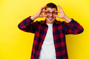 Young caucasian cool man isolated on yellow background showing okay sign over eyes