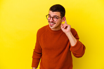 Young caucasian cool man isolated on yellow background trying to listening a gossip.