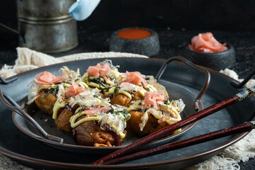 traditional Japanese octopus takoyaki  presented on a rustic metal tray with pickled ginger and spicy sauce. in a dark background.