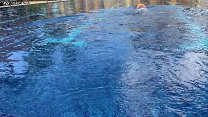 Middle aged male swimming free style in a crystal clear, blue pool between lap lanes