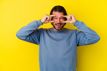 Middle age caucasian man isolated on yellow background showing okay sign over eyes