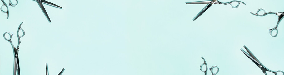 Banner flat lay from above of professional silver hair cutting shears set on green background. Hairdresser salon equipment and haircut work tools concept during quarantine with copy space