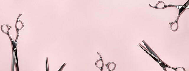 Banner flat lay from above of professional silver hair cutting shears set on pink background. Hairdresser salon equipment and haircut work tools concept during quarantine with copy space