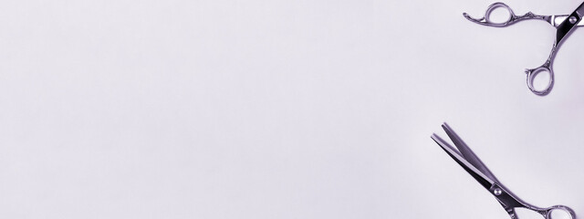 Banner flat lay from above of professional silver hair cutting shears set on purple background. Hairdresser salon equipment and haircut work tools concept during quarantine with copy space