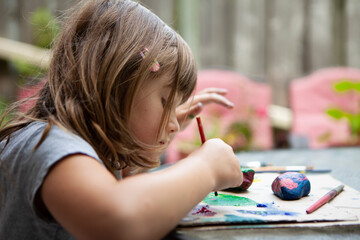 Young Girl paints Rocks outside on Patio Table