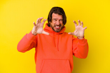 Middle age caucasian man isolated on yellow background showing claws imitating a cat, aggressive gesture.