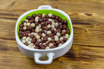 Cereal chocolate balls with milk in a bowl on wooden table