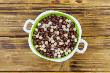 Cereal chocolate balls with milk in a bowl on wooden table. Top view