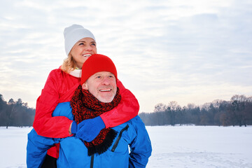 Smiling senior man giving mature woman piggyback in snowy winter park. Active lifestyle after...
