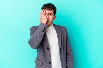 Young caucasian man isolated on blue background having fun covering half of face with palm.