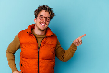 Young caucasian man wearing eyeglasses isolated on blue background smiling cheerfully pointing with forefinger away.