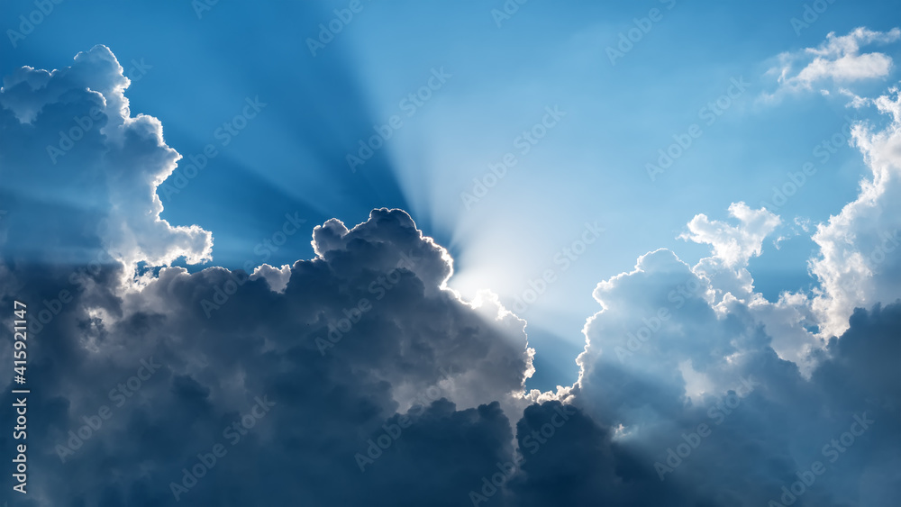 Wall mural sun behind dark clouds with sun rays on blue sky background