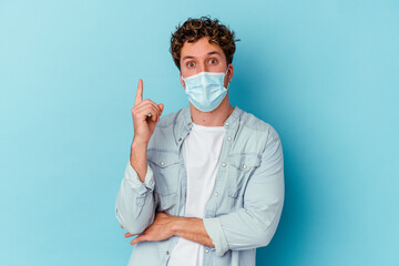 Young caucasian man wearing an antiviral mask isolated on blue background having some great idea, concept of creativity.
