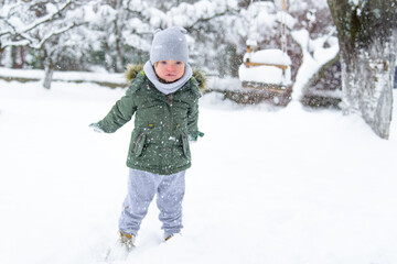 Fototapeta na wymiar Down syndrome toddler boy throws snowflakes from his hands. Blurred. Disabled boy enjoys the frosty winter weather and snow. Winter fun in the yard. Frosty weather. Winter breath. Snow explosion