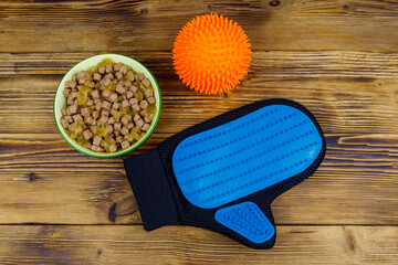 Canned dog food in bowl, ball toy and pet grooming glove on wooden background. Top view. Pet care concept