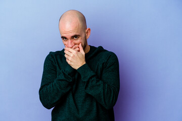 Young caucasian bald man isolated on purple background covering mouth with hands looking worried.
