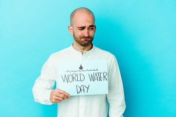 Young caucasian bald man celebrating world water day isolated on blue background confused, feels doubtful and unsure.