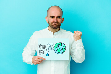 Young caucasian bald man celebrating world water day isolated on blue background showing fist to camera, aggressive facial expression.