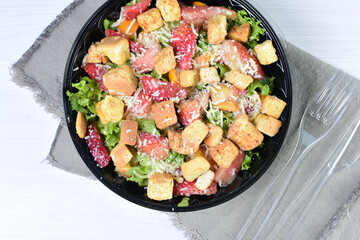 Rich very colorful vegetable salad, with croutons, strawberries, lettuce, Parmesan cheese and cherry tomato on white wooden background