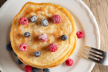 Stack of pancakes with fresh berries on a white plate on the table, top view
