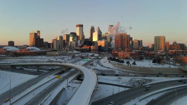 Minneapolis downtown skyline aerial footage during a winter golden hour, highways covered with snow, transportation during rush hour