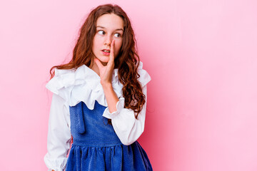 Little caucasian girl isolated on pink background is saying a secret hot braking news and looking aside