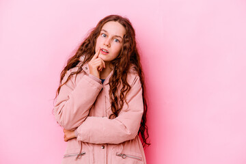 Little caucasian girl isolated on pink background looking sideways with doubtful and skeptical expression.
