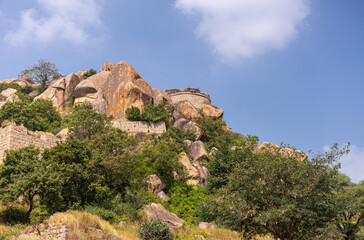 Chitradurga, Karnataka, India - November 10, 2013: Fort or Elusuttina Kote. Half circle rampart on top of boulder rock hill with more walls lower, green foliage under blue cloudscape.
