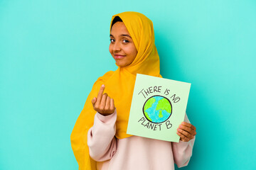 Young muslim woman holding a there is not planet b placard  isolated on blue background pointing with finger at you as if inviting come closer.