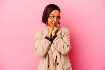 Young business mixed race woman isolated on pink background keeps hands under chin, is looking happily aside.