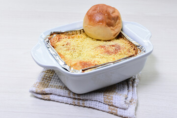 Meat lasagna, with lots of Parmesan cheese, accompanied by bread on a white wooden bottom