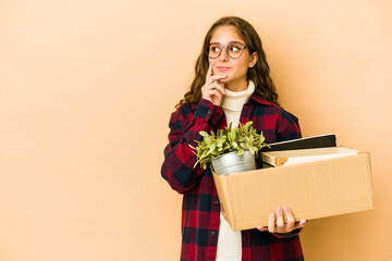 Young caucasian woman moving holding a box isolated looking sideways with doubtful and skeptical expression.