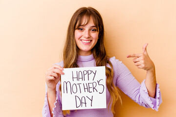 Fototapeta na wymiar Young caucasian woman holding a Happy mothers day placard isolated person pointing by hand to a shirt copy space, proud and confident
