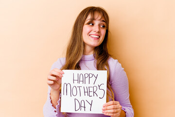 Fototapeta na wymiar Young caucasian woman holding a Happy mothers day placard isolated looks aside smiling, cheerful and pleasant.