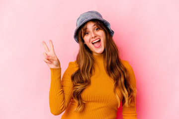 Young caucasian woman wearing fishermans hat isolated joyful and carefree showing a peace symbol with fingers.