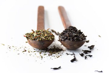 Black and green loose leaf teas in wooden spoons isolated on white background