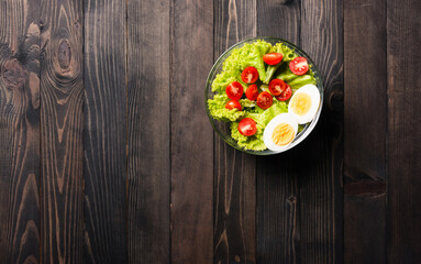 Top view of the healthy colorful salad bowl with tomatoes fresh mixed greens vegetable in a dish on black wooden background, Health salad snack food concept