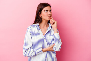 Young caucasian woman isolated on pink background thinking and looking up, being reflective, contemplating, having a fantasy.