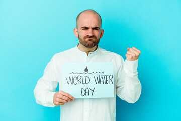 Young caucasian bald man celebrating world water day isolated on blue background showing fist to camera, aggressive facial expression.
