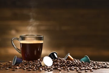 Fotobehang Cup glass of coffee with smoke and coffee beans and coffee capsule on old wooden background © amenic181