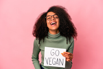 Young african american curly woman holding a go vegan placard laughing and having fun.