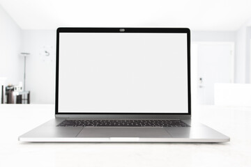 Laptop open with blank screen on a white table at workplace with blurred bright sunlight through the window, front view. Work from home concept with minimal modern home, depth of field.
